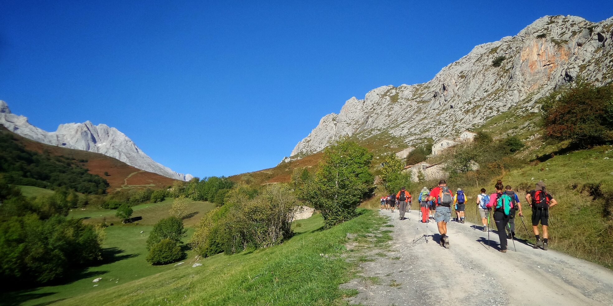 The hikers walking through a pathway surrounded by hills covered in greenery under the sunlight at daytime